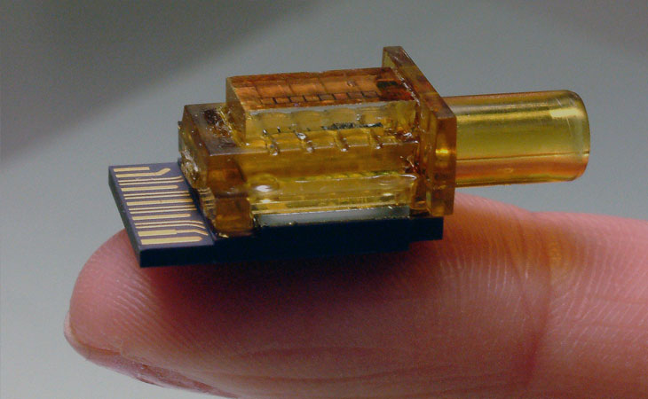 Inneos | Fiber Optic Components – Made in the USA An orange optical subassembly (OSA) resting on someone's finger tip.