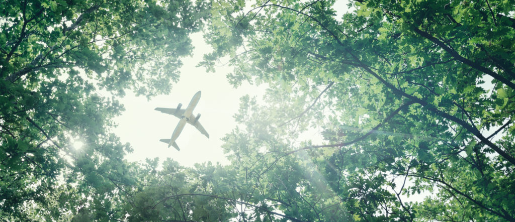 Inneos | Exploring the Hidden Benefits of Using Fiber Cables in Electric Aircraft A plane flying in the sky against a background of green trees. Eco-friendly electric aircraft concept.
